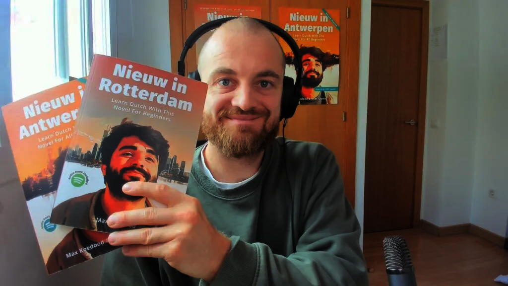 Taalcoach Max Keesdoorn poseert met zijn boeken Nieuw in Rotterdam en Nieuw in Antwerpen — romans bedoeld voor beginners die Nederlands leren, inclusief audio via Spotify.